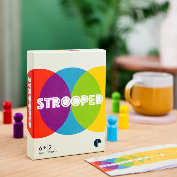 Strooped box standing on a table with the cards spread in front and the 5 coloured pawns scattered.