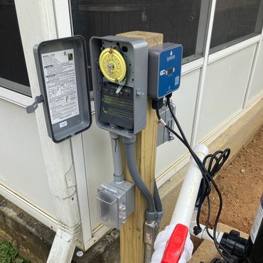 Outdoor electrical setup with timers, outlets, and wiring on a wooden post.