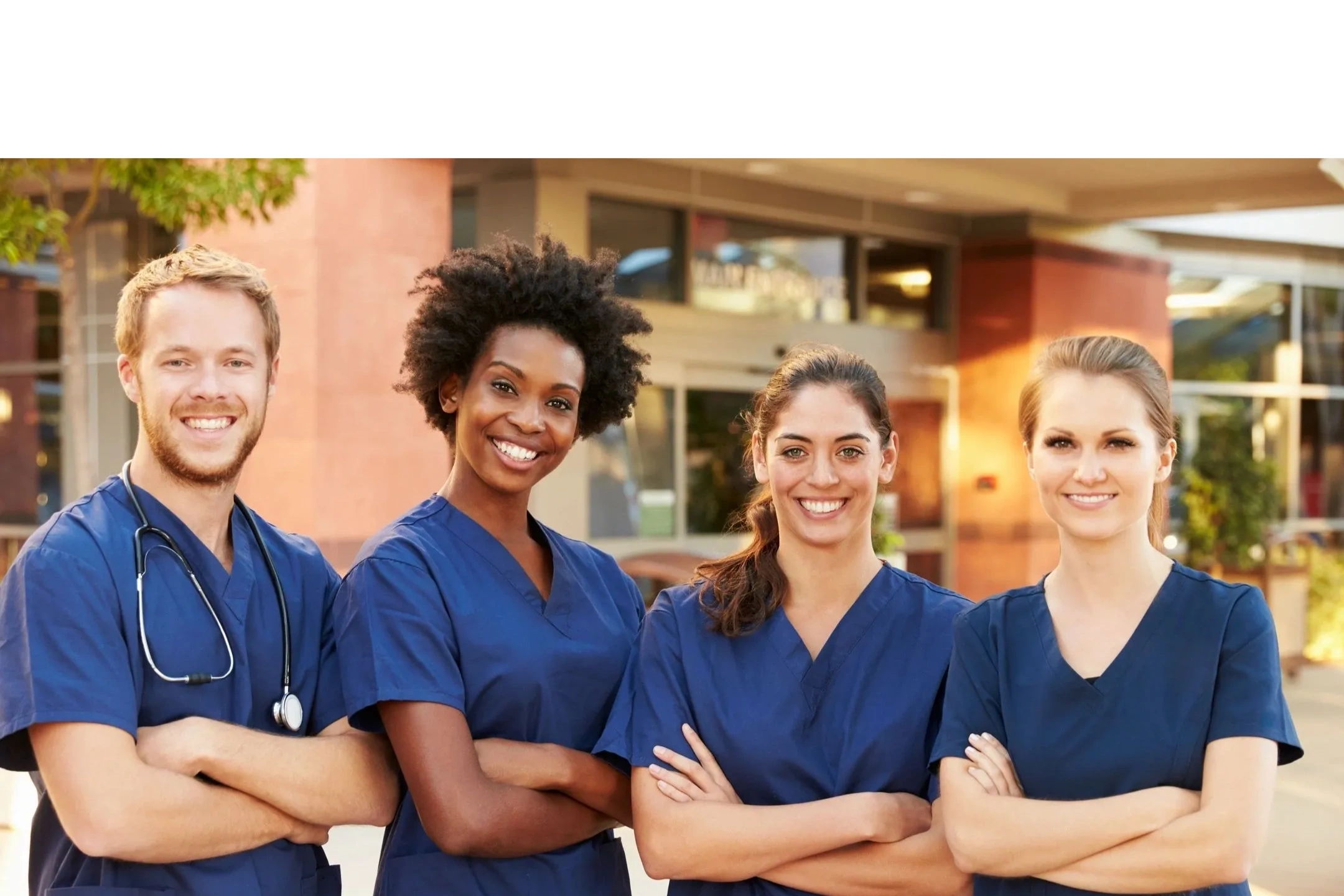 Four healthcare professionals in blue scrubs smiling outside a medical facility.