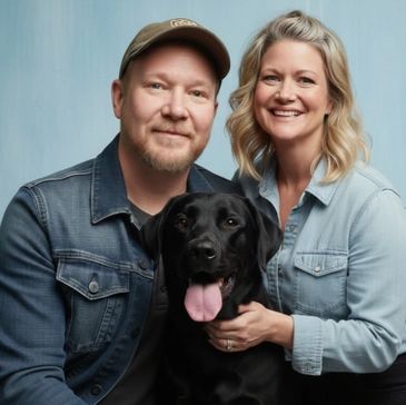 Happy couple with their black dog smiling at the camera.