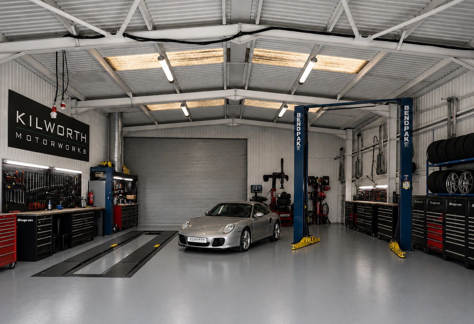 A silver sports car inside a clean garage with tools and tires.