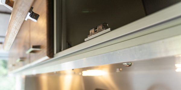 Close-up of a kitchen cabinet with a latch and under-cabinet lighting.