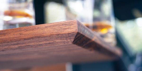 Close-up of a wooden table corner with blurred glasses in the background.
