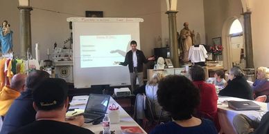 A man gives a presentation to a seated audience in a church setting.
