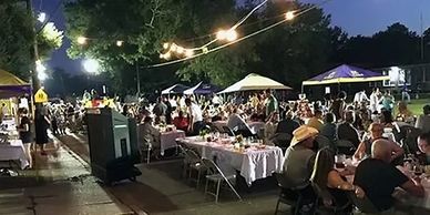 Outdoor evening event with people dining under string lights and tents.