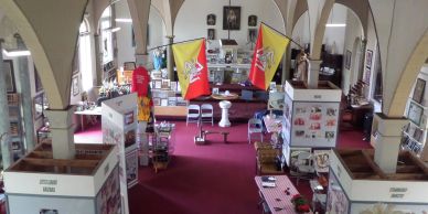 Interior of a museum or exhibition hall with flags, displays, and tables.