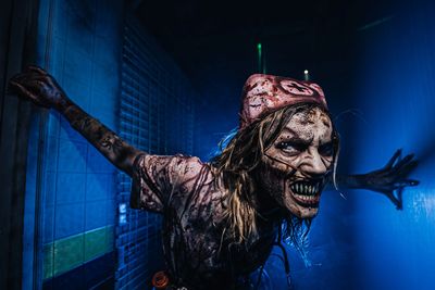 Terrifying zombie nurse leans forward in dark, eerie hallway.