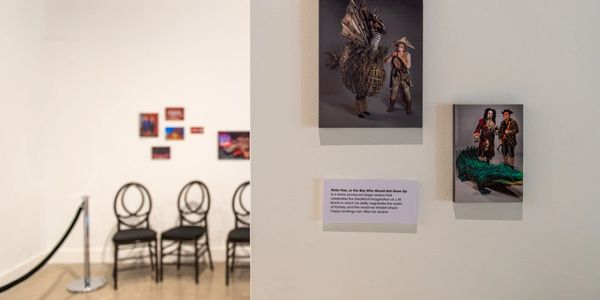 Art exhibit featuring detailed costume photographs and empty chairs in a gallery space.