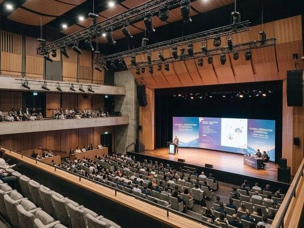 Speaker addressing audience at a symposium in a large auditorium.