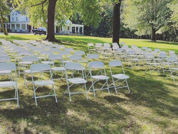 Rows of white folding chairs set up outdoors on a sunny day.