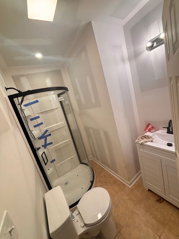 Small bathroom under renovation with a shower, toilet, and sink.