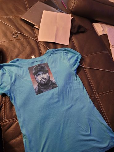 Blue T-shirt with a stylized portrait of a man wearing a cap on a leather couch.