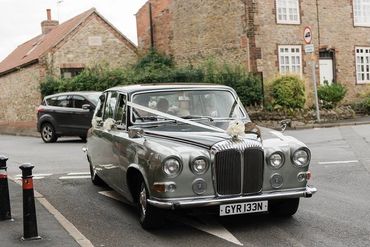 A 1974 Daimler DS420 driving to a wedding with white ribbons