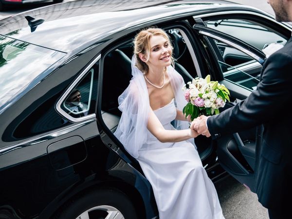 a groom in a suit giving hand to an attractive and smiling bride with a bouquet