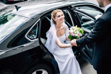 A bride being helped out of the back of her wedding car limousine