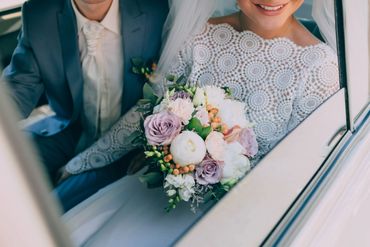 A bride holding flowers in the back of a classic limousine wedding car