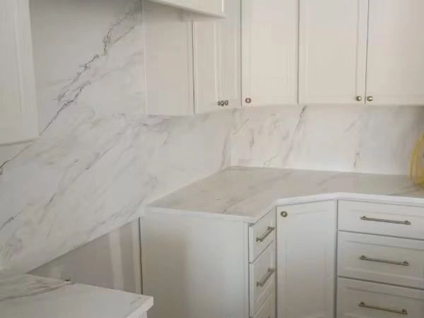 White kitchen cabinets with marble countertops and backsplash.