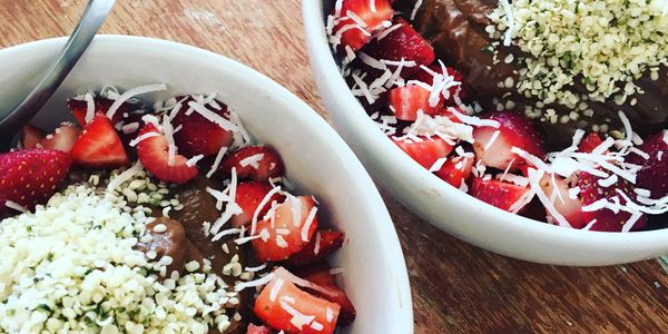Two bowls of chocolate smoothie topped with strawberries, shredded coconut, and seeds.
