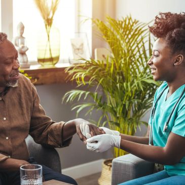 Nurse checking elderly man's hand with a smile.