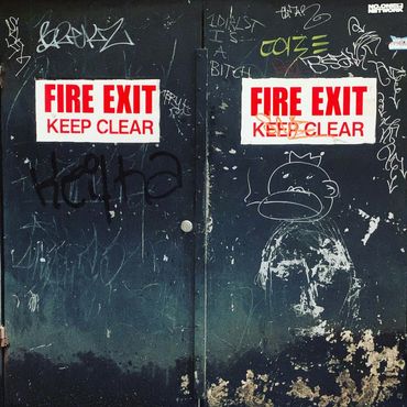 Double black fire exit doors with graffiti and white 'FIRE EXIT KEEP CLEAR' signs.