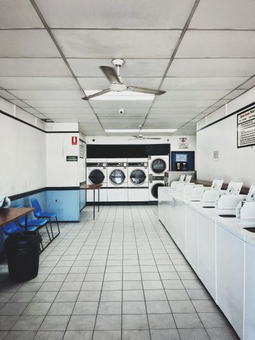 Empty laundromat with washing machines, dryers, and blue chairs.