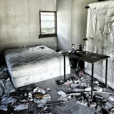 Messy, abandoned room with a dirty mattress and scattered trash on the floor.