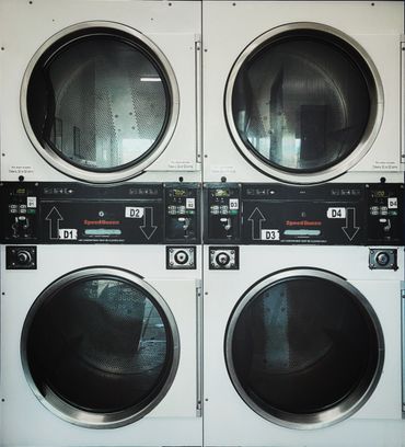 Four stacked industrial laundry dryers in a laundromat setting.