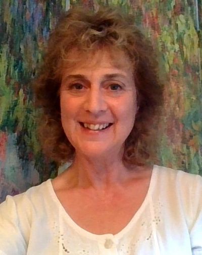Smiling woman with curly hair in a white top against a colorful background.