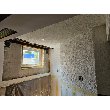 Basement window area under renovation with textured walls and plastic sheeting.