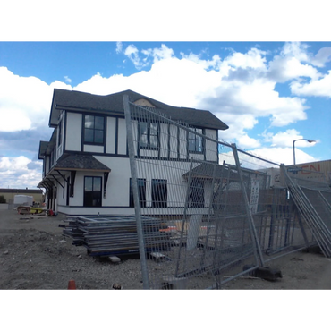 A two-story house under construction behind temporary metal fencing.