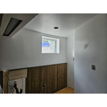 A small room with a window, wood paneling, and plumbing fixtures.