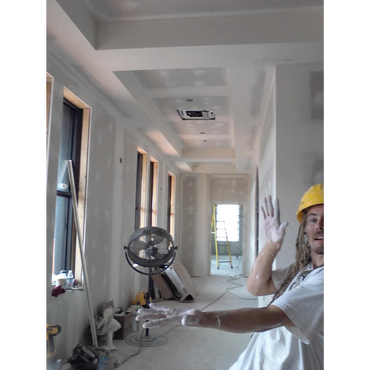 Construction worker with paint-covered hands posing inside a room under renovation.