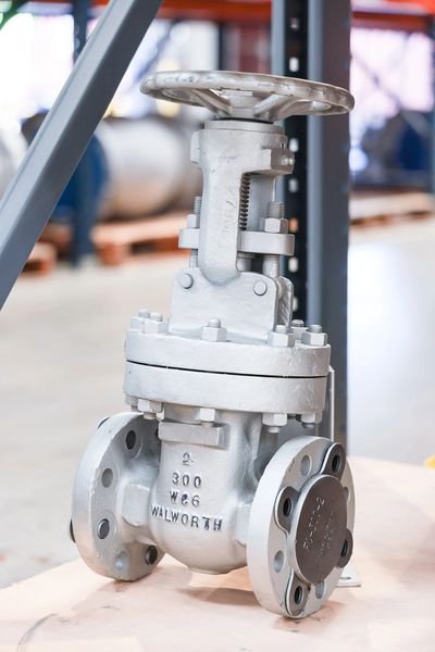 A metallic industrial valve with a wheel handle in a workshop setting.