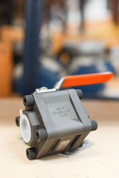 Industrial metal valve with an orange handle on a blurred background.