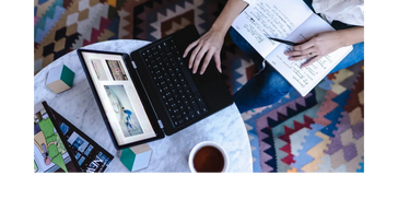 Picture of a woman working on a laptop with a notebook on her lap.