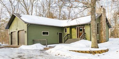 Green house with snow-covered roof and surrounding trees in winter.