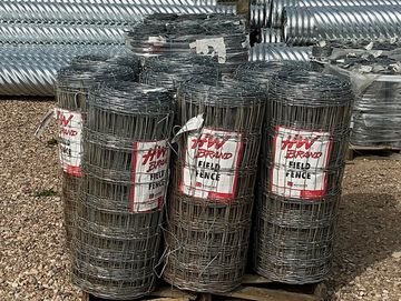 Rolls of field fence wire stacked outdoors on a pallet.