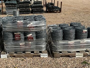 Pallets of coiled fencing wire wrapped in plastic outdoors.