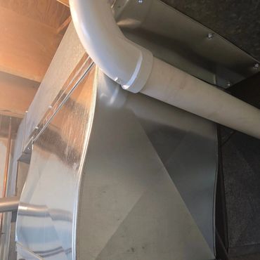 Metal HVAC ductwork with a white plastic pipe attached in a utility room.