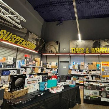 Electronics and tech gadgets displayed in a store with signs for suspension and tires & wheels.