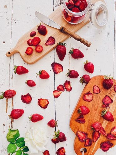 Fresh and sliced strawberries with a white rose on a rustic wooden table.