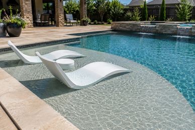 Modern pool with curved white lounge chairs in shallow water area.