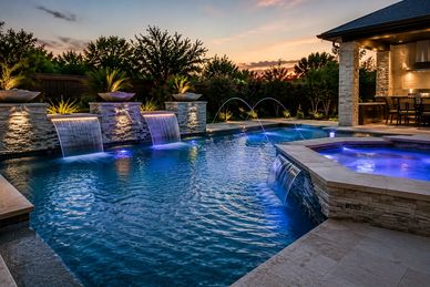Luxury backyard pool with waterfalls and ambient lighting at sunset.