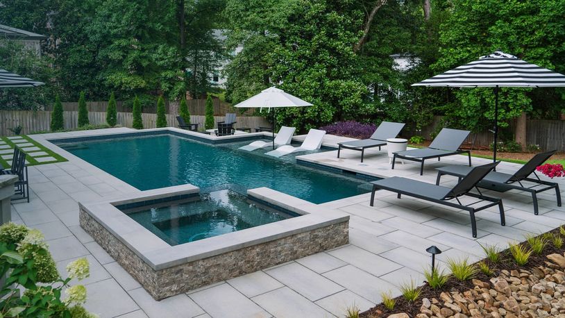 Modern backyard pool with lounge chairs and umbrellas amid lush greenery.