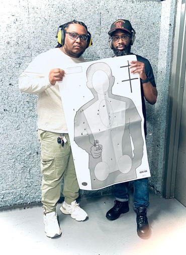 Two men at a shooting range holding a bullet-riddled target sheet.