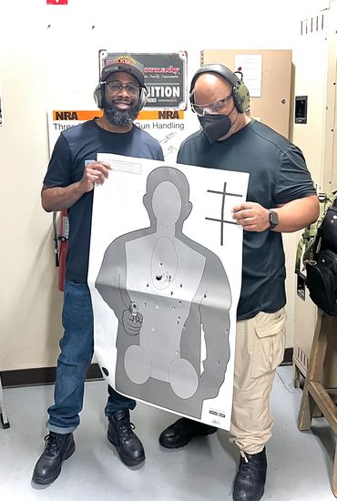 Two men at a shooting range holding a bullet-riddled target poster.