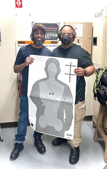 Two men holding a target sheet with bullet holes at a shooting range.