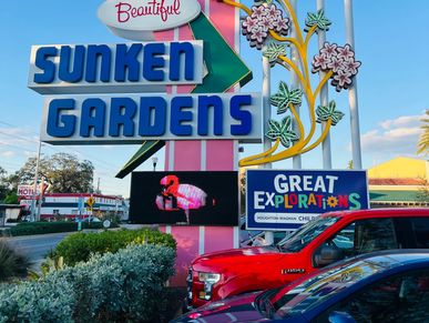 Sunken Gardens sign with colorful decorations and cars in front.