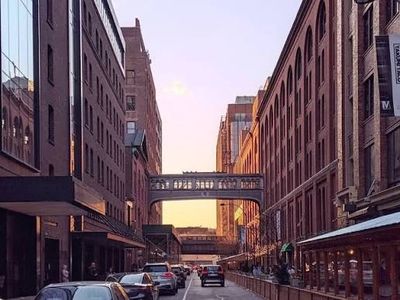 Sunset view of an urban street with a glass pedestrian bridge between brick buildings.