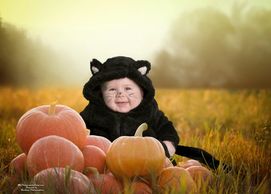 A baby in costume next to pumpkins